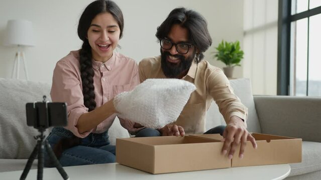 Couple bloggers customers open package box order online shopping delivery excited happy Arabian man and woman record blog stream on mobile phone at home open parcel win digital tablet unpacking video