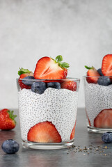 Chia pudding with coconut milk and berries. Strawberry chia pudding in glasses on a gray background. Healthy food concept. Copy space.