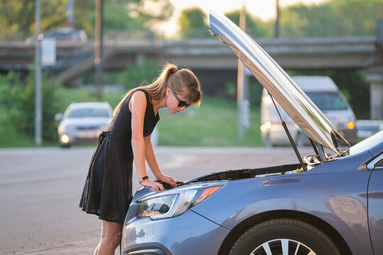 Helpless woman standing near her car with open bonnet inspecting broken motor. Young female driver having trouble with vehicle