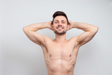 Attractive smiling young man isolated on gray background. Having two arms behind the head, showing his armpits
