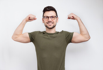 Young strong man in glasses and casual t-shirt showing biceps