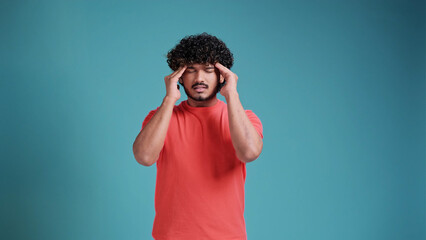Young handsome latin spanish man on blue studio background with hand on head for pain in head. Suffering migraine.