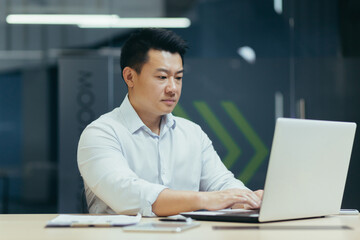 Fototapeta na wymiar A young man of Asian origin programmer, developer works in the office at a desktop using a laptop.