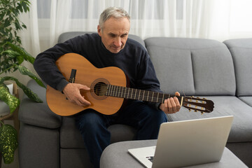 an elderly man learns to play the guitar on a laptop
