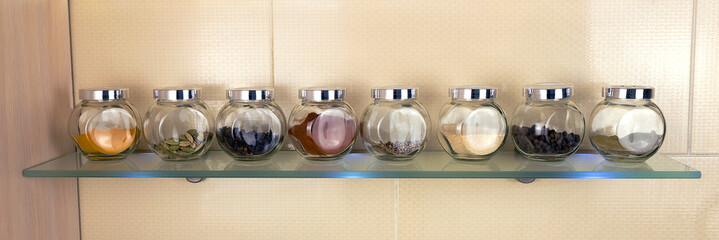 A set of dried spices in glass jars displayed on a shelf in the kitchen. Cooking concept.