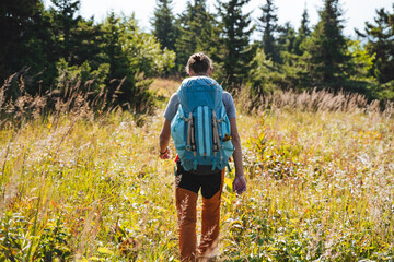 A man walks alone on a trail in an autumn forest, a large hiking backpack on his back, a hipster on a hike, an autumn forest tall grass, a sports hike.