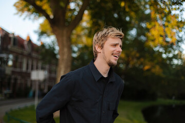 Young fun man wear black shirt and t-shirt walking rest relax in spring or summer green city park go down alley sunshine lawn outdoors on nature. Urban lifestyle leisure concept. Blonde man laughing