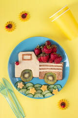 Obraz na płótnie Canvas Healthy toast for kids in shape of car with strawberry, kiwi and cheese on blue plate on yellow background