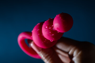 Woman holding pink anal beads in drops of water on a blue background. Sex toy hygiene concept.