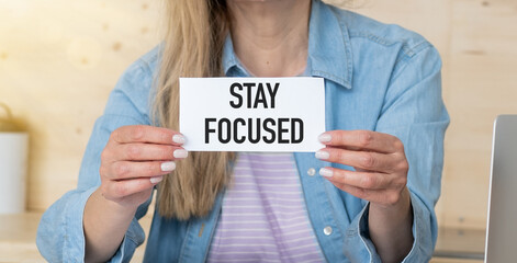 Stay focused text on blank business card being held by a woman's hand with blurred background.