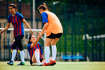 Soccer player assists her teammate in getting up after foul on playing field.