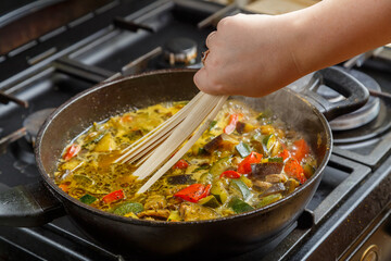 Frying pan with stewed vegetables in sauce and spices female hand puts udon.