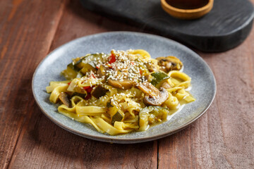 plate with udon vegetables mushrooms and sesame seeds on a wooden table.