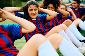 Women's soccer team practicing sit-ups during sports training on playing field. - Powered by Adobe