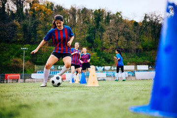 Athletic woman leading ball around cones during soccer training on playing field.