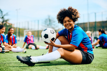 Happy black athletic woman with soccer ball on playing field looking at camera. © Drazen