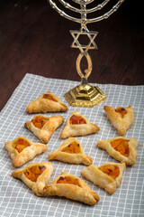 Homemade gomentashi cookies for the Jewish holiday of Purim on a checkered napkin next to the menorah.
