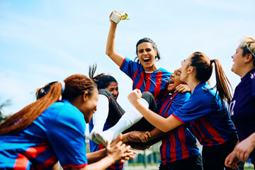 Excited female soccer players have fun while celebrating winning tournament trophy.