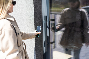 Woman puts the smart phone to the electronic reader to access the apartment or office. Cell with...