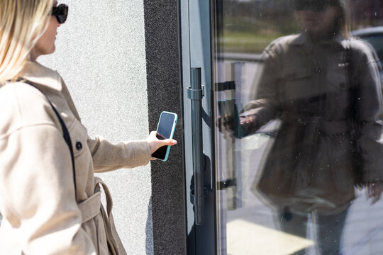 Woman puts the smart phone to the electronic reader to access the apartment or office. Cell with running mobile secure application