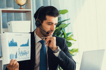 Business man wearing headphone present financial data or BI paper via laptop during online meeting....