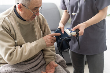 Young woman doctor wearing white uniform with stethoscope checking mature patient blood pressure at meeting in hospital, serious physician gp using digital tonometer.