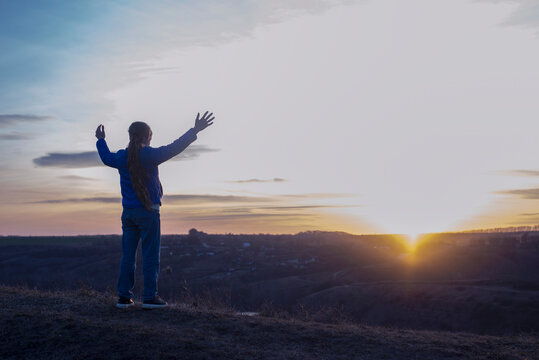A girl with raised hands on the background of the sky. Prayer. Glorification of God. Worshiping Jesus