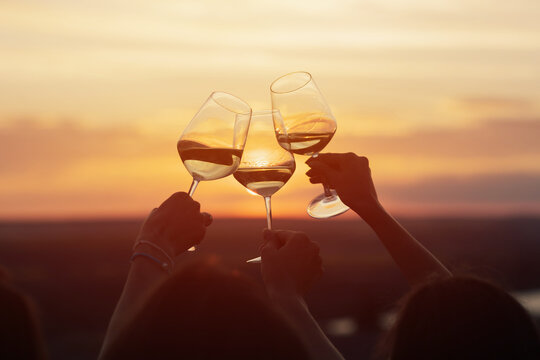 A group of girlfriends raise a toast with glasses of white wine on a sunset. Close shot.	