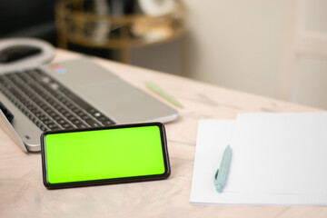 Horizontal cell phone with chroma key or green screen over a desk with a laptop and sheets