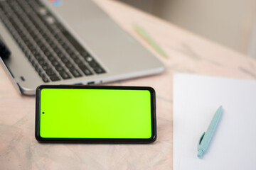 Horizontal cell phone with chroma key or green screen over a desk with a laptop and sheets