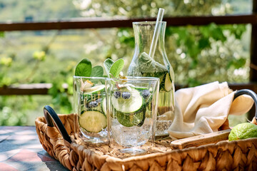 Refreshing summer drink - cucumber infused water with ice, sage, cucumber and lemon blossom on the table in the garden. Fresh healthy cold detox beverage. Fitness drink.