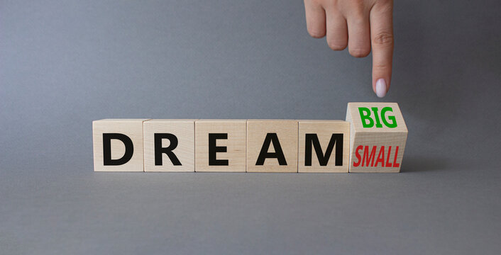 Dream Big vs Small symbol. Businessman Hand points at wooden cubes with words Dream Small and Dream Big. Beautiful grey background. Business and Dream concept. Copy space