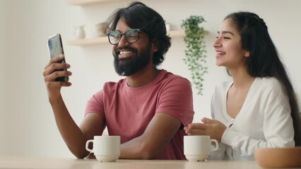 Multiethnic arabian indian couple in kitchen talking mobile phone webcam application happy woman and man hold video call conversation waving hands use cellphone communicate meeting online with friends