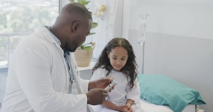 Happy diverse doctor examining girl with otoscopy in hospital in slow motion