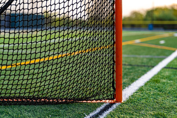 Dramatic late afternoon photo of a lacrosse goal on a synthetic turf field before a night game.
