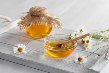Chamomile syrup in a small bowl and in a jar on a white wooden table