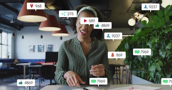 Animation of social media icons over african american woman having a video call at office