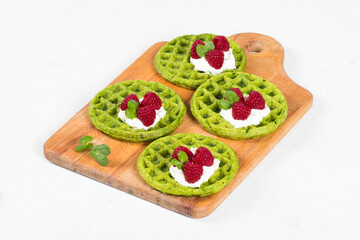 Round spinach waffles with raspberries, on a wooden board. White background
