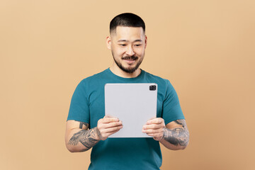 Smiling asian man using digital tablet isolated on beige background. Successful businessman online shopping