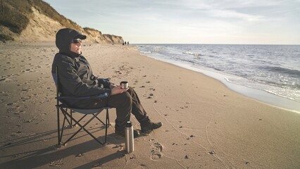 rest on the shore, a man on a chair with a thermos of tea