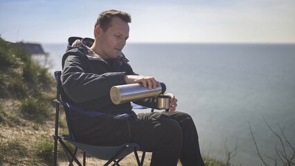 man drinking tea from a thermos on the background of the sea