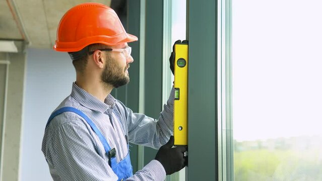 Builder measures of the vertical deviation of pvc windows. A repairman in uniform installs pvc windows in new office