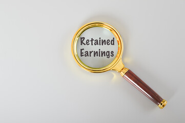 Magnifying glass written with RETAINED EARNINGS isolated on a grey background.