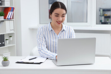 Young female intern working with laptop at table in office