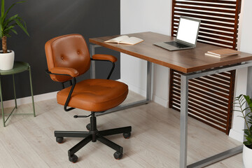Stylish office interior with comfortable chair, desk and laptop