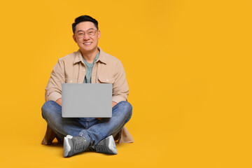 Happy man with laptop on yellow background, space for text