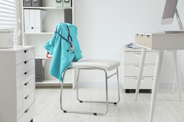 Turquoise medical uniform and stethoscope hanging on chair in clinic