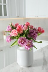 Beautiful bouquet of colorful tulip flowers on white marble table in kitchen