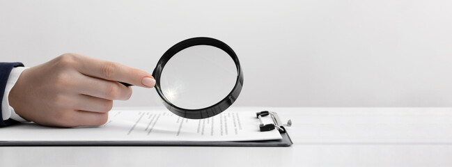 Woman looking at documents through magnifier at white table, closeup. Banner design with space for...