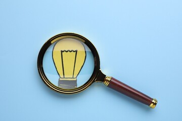 Magnifying glass over paper light bulb on blue background, top view